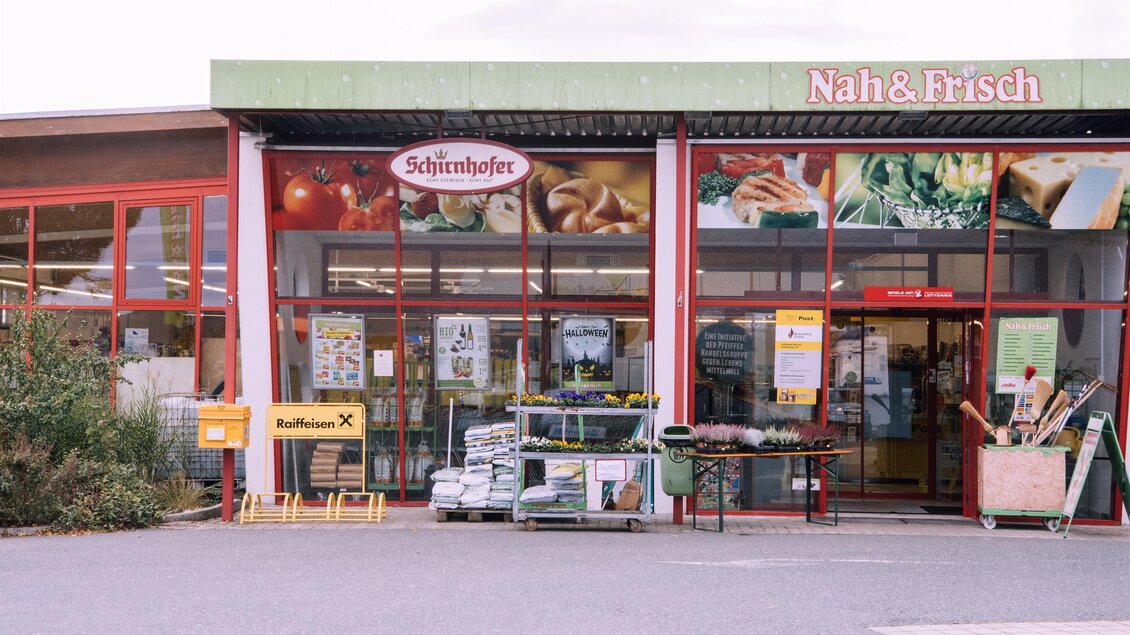 Ein Lebensmittelladen mit einem eingängigen Geschäftsnamen. Vor der Tür stehen Einkaufswagen und verschiedene Waren. | © Kurkommission Bad Blumau