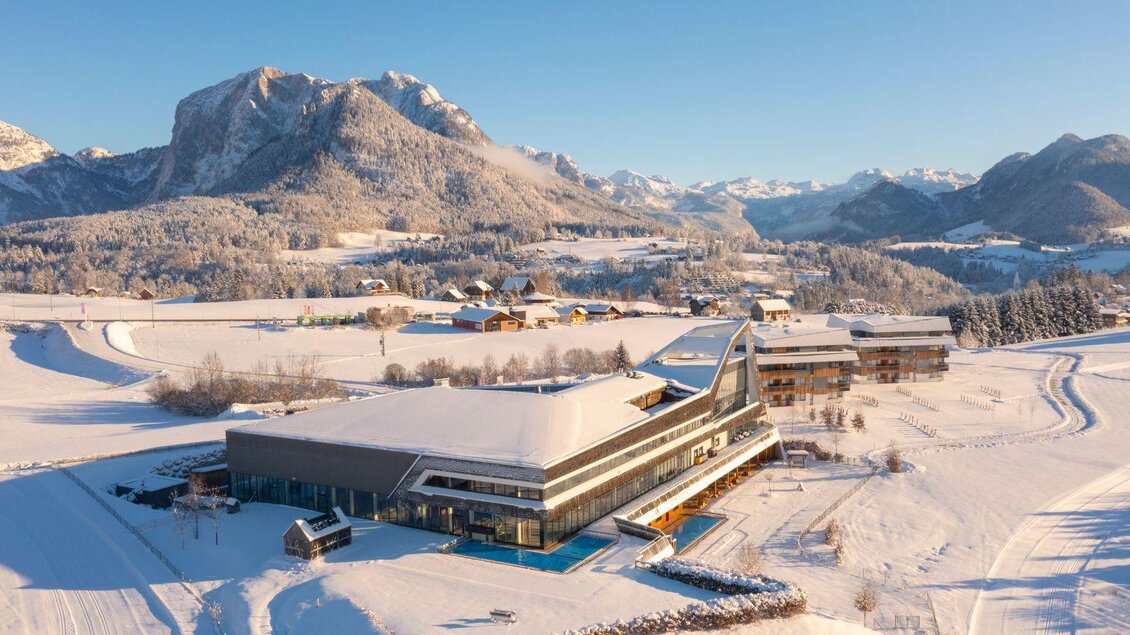 Ein modernes Gebäude in einer verschneiten Landschaft mit Bergblick. Die Umgebung ist idyllisch und ruhig, mit schneebedeckten Feldern und kleinen Hütten. | © Thomas Lahnsteiner