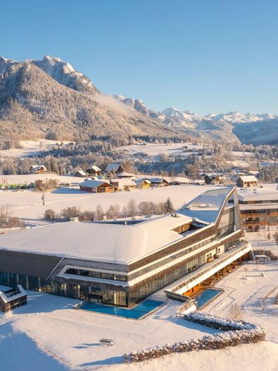 A modern building in a snowy landscape with mountain views. The surroundings are idyllic and quiet, with snow-covered fields and small cottages. | © Thomas Lahnsteiner