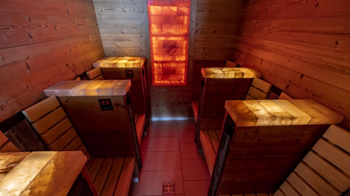 Ein moderner Wellnessbereich mit Holzbänken und sanfter Beleuchtung. Im Raum befindet sich eine Salzsteinallee und eine entspannende Atmosphäre.