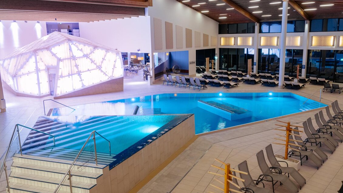 Ein moderner Innenpool mit klarem Wasser und einem Bereich zum Entspannen. Liegen stehen bereit, um die Umgebung zu genießen. | © Karl Steinegger