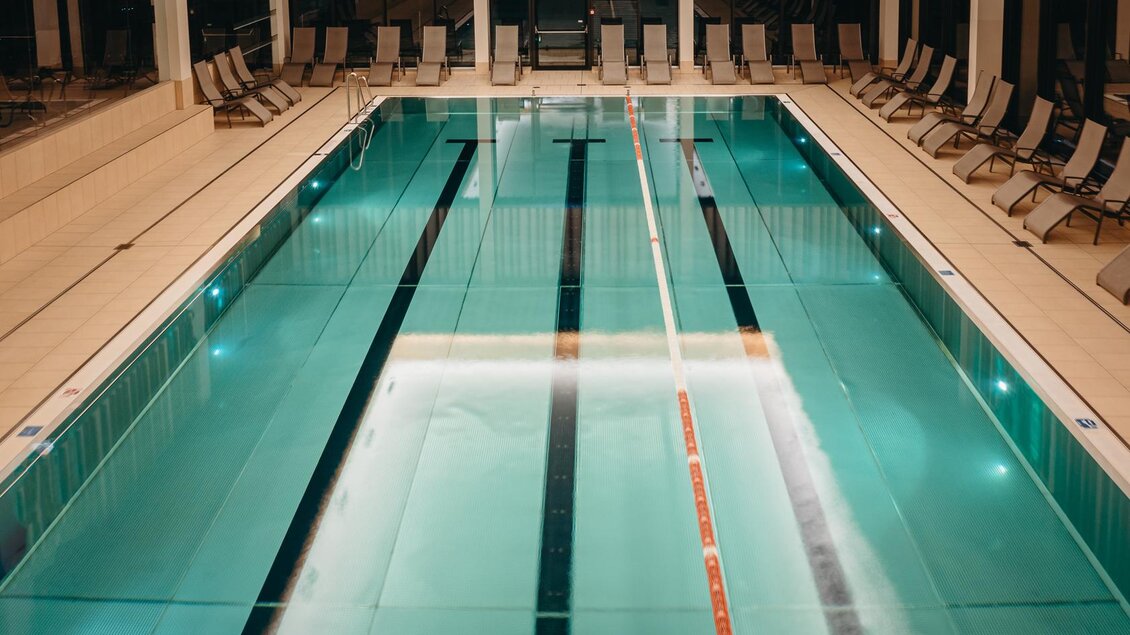 Ein elegantes Schwimmbad mit glasklarem Wasser und bunten Schwimmbahnen. Umgeben von komfortablen Liegen für Entspannung. | © Karl Steinegger