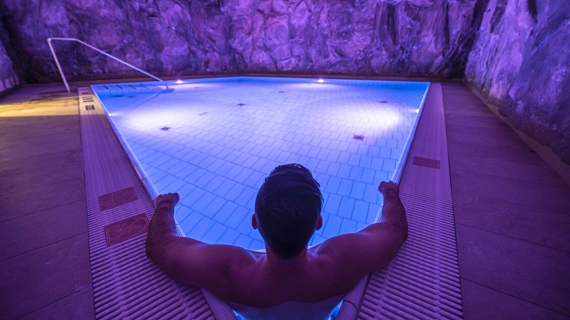 Ein Mann entspannt am Rand eines beleuchteten Pools in einer Höhle. Die sanfte blaue Beleuchtung schafft eine ruhige Atmosphäre. | © Thomas Lahnsteiner