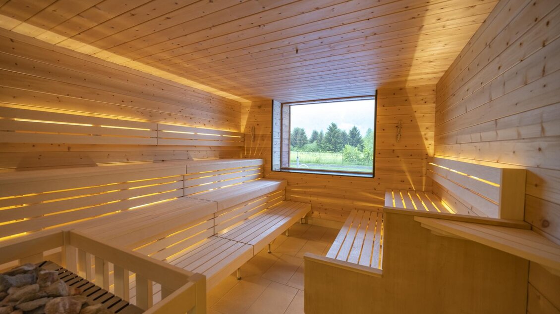 Eine moderne Sauna mit Holzinterieur und sanfter Beleuchtung. Durch das Fenster blickt man auf eine grüne Landschaft. | © Thomas Lahnsteiner