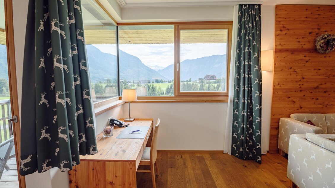 Ein gemütlicher Raum mit einem Holzschreibtisch und einem Fenster, das einen Blick auf die Berge bietet. Die Vorhänge haben ein tierisches Muster und die Einrichtung ist modern und einladend.