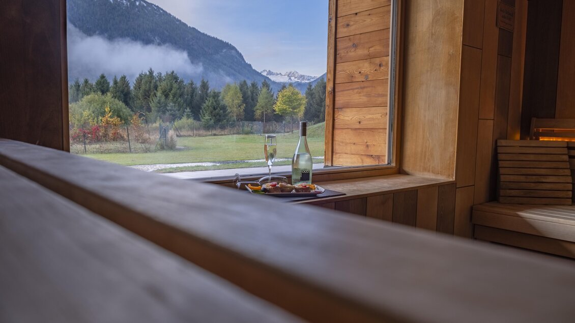 Eine gemütliche Innenansicht mit einem Fenster, das auf eine malerische Berglandschaft blickt. Auf der Fensterbank stehen Gläser und eine Flasche, die zu einem entspannenden Moment einladen.