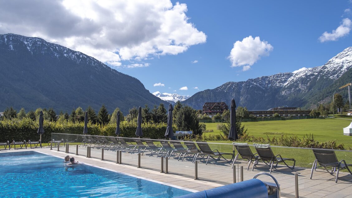 Ein schöner Pool mit Blick auf majestätische Berge. Die Landschaft ist grün und einladend unter einem blauen Himmel.