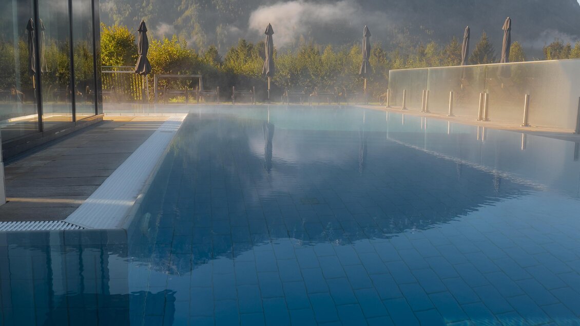 Ein moderner Infinity-Pool mit klarem Wasser und Blick auf die Berge. Die Umgebung ist ruhig und grün, mit leichtem Nebel in der Luft.