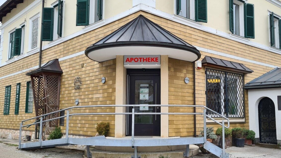 Eine Apotheke in einem modernen Gebäude mit einem Eingang und Rampen. Die Fassade ist aus Holz und hat grüne Fensterläden. | © Stephanie Bor