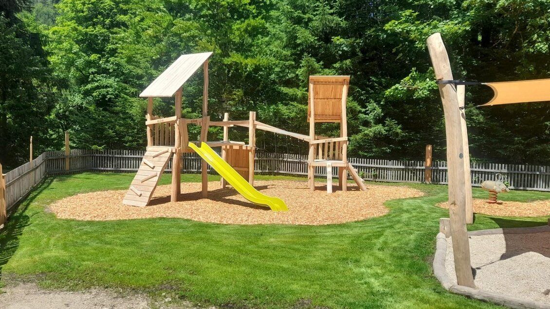 Ein schöner Spielplatz mit einer Rutsche und Klettergerüst aus Holz. Umgeben von grünem Gras und Bäumen. | © Isabell Schachner
