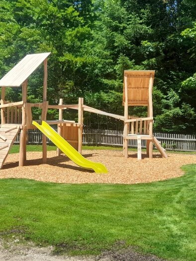 A beautiful playground with a slide and a wooden climbing frame. Surrounded by green grass and trees. | © Isabell Schachner
