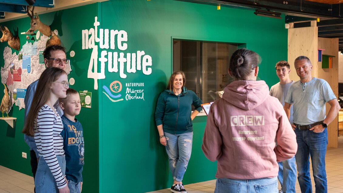 Eine Gruppe von Menschen steht in einem Raum mit grünen Wänden und einem großen Wandbild. Sie lächeln und scheinen ein Gespräch zu führen. | © Naturpark Mürzer Oberland