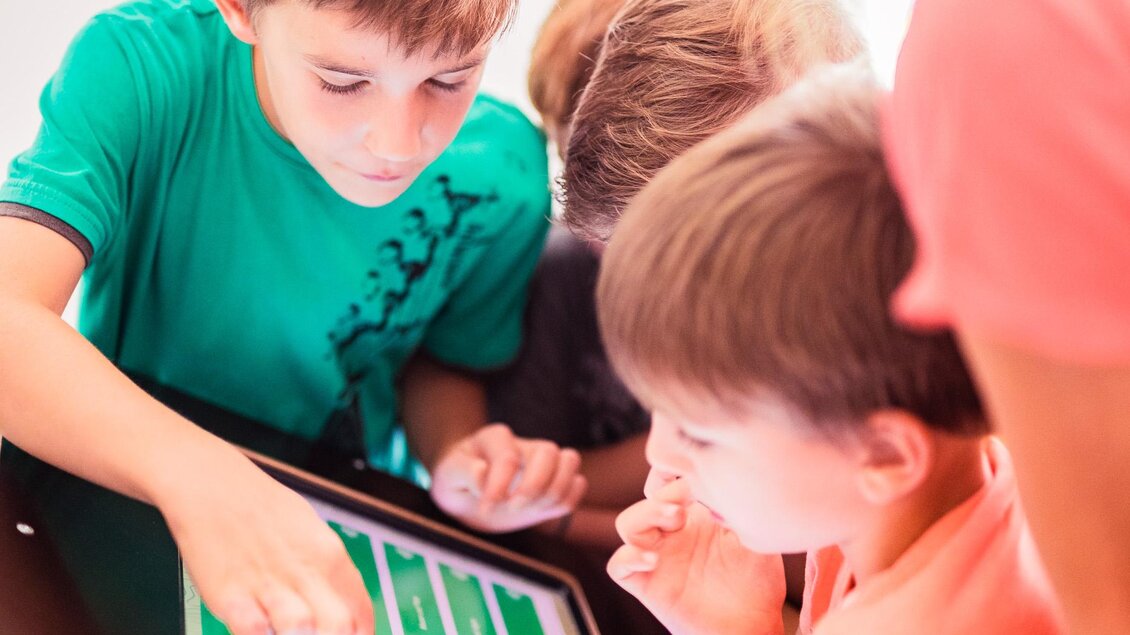 Eine Gruppe von Kindern und einer Erwachsenen schaut konzentriert auf einen Bildschirm. Sie interagieren mit einem digitalen Inhalt. | © Tourismusverband Murau