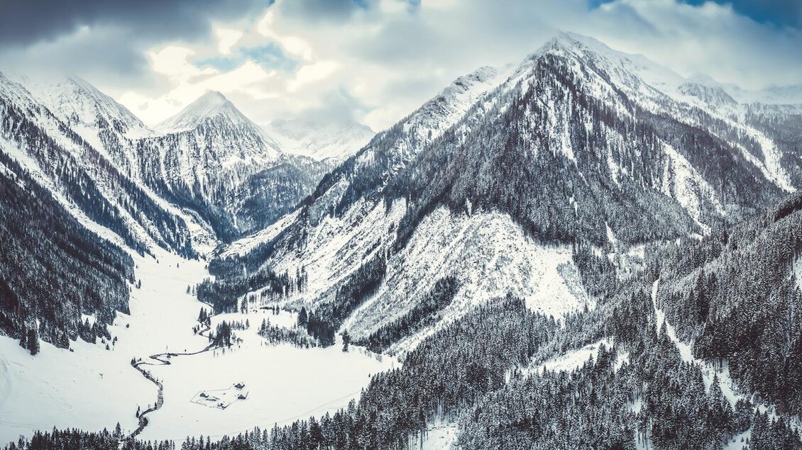 Eine winterliche Berglandschaft mit schneebedeckten Gipfeln und einem tiefen Tal. Der Himmel ist bewölkt und es gibt Schnee auf den Bäumen. | © Christoph Huber