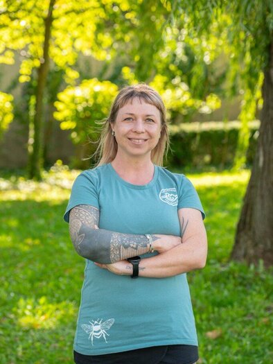 Eine lächelnde Frau sitzt vor einem Hintergrund mit einer grünen Wiese. Sie trägt ein grünes T-shirt und wirkt freundlich. | © Helmut Schweighofer