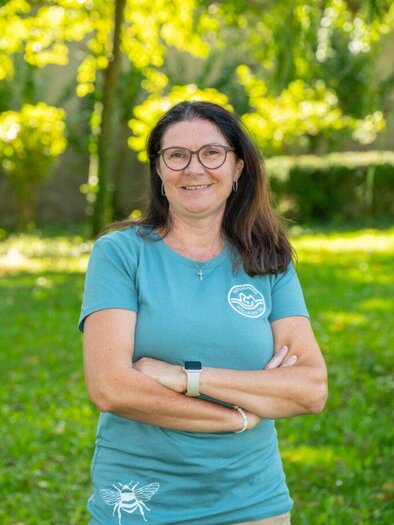 A smiling woman sits in front of a background with a green meadow. She is wearing a green T-shirt and appears friendly. | © Helmut Schweighofer