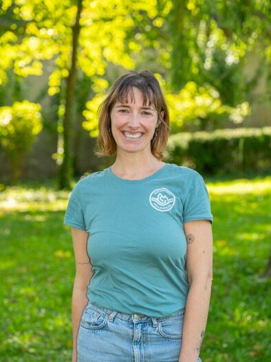 A smiling woman with glasses is wearing a light sweater. In the background, plant images can be seen. | © Helmut Schweighofer