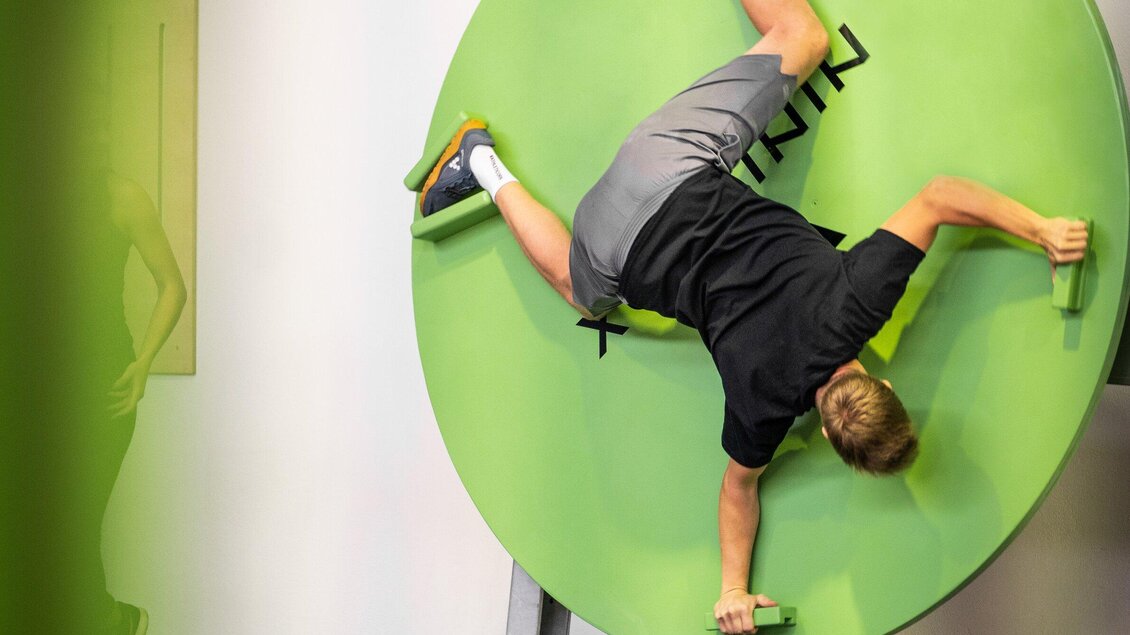 <p>Junger Mann klettert an einer Trainingsscheibe  in der Ninjabox Graz, indem er sich mit speziellen Griffen festhält und die Balance hält.</p> | © Ninjabox_5