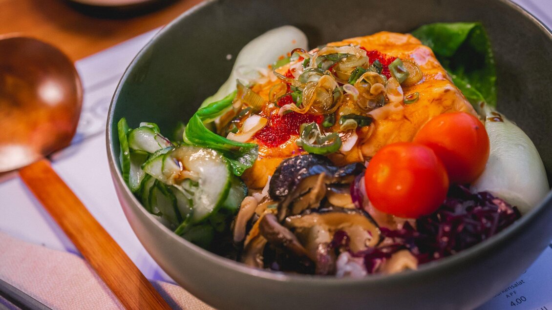 Eine Schüssel mit buntem Essen, bestehend aus Gemüse, Reis und einer deutlich sichtbaren Portion Lachs. Frische Zutaten und lebendige Farben machen das Gericht appetitlich. | © Moriwano Group - jack-coleman