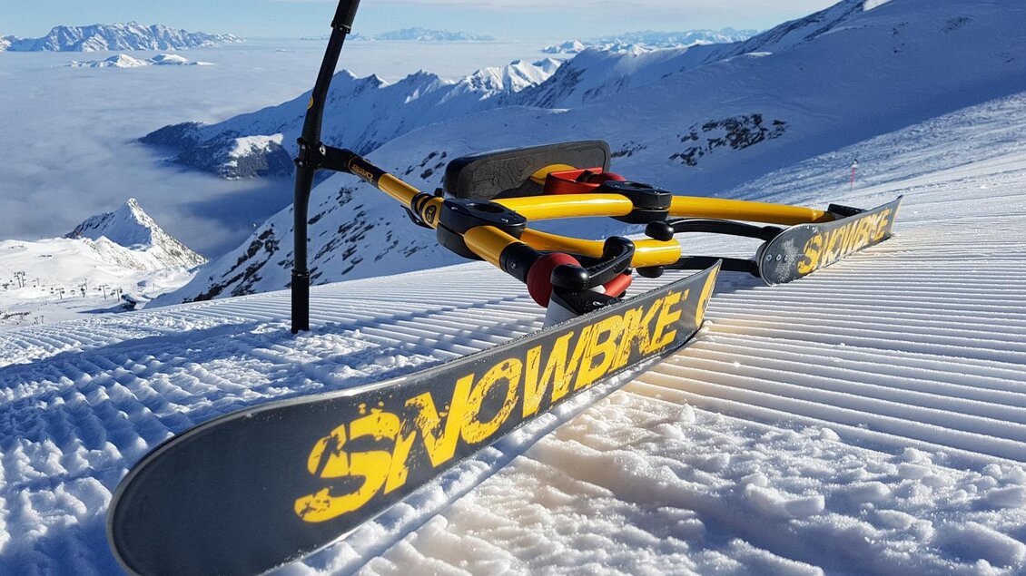 Ein schneesicherer Berg mit einem Snowbike und frischen Pisten. Im Hintergrund sind beeindruckende Berge und ein klarer Himmel zu sehen. | © Thomas Humer