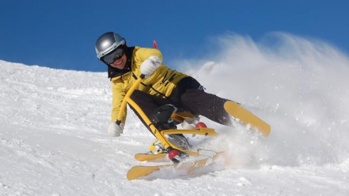 Eine Person in gelber Skijacke fährt auf einer schneebedeckten Piste. Der Himmel ist klar und blau, während Schnee aufwirbelt. | © Thomas Humer