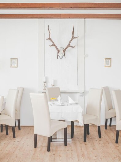 A bright, inviting restaurant with light tables and chairs. Decorative pictures and a antler hang on the wall. | © OLIVER kocht