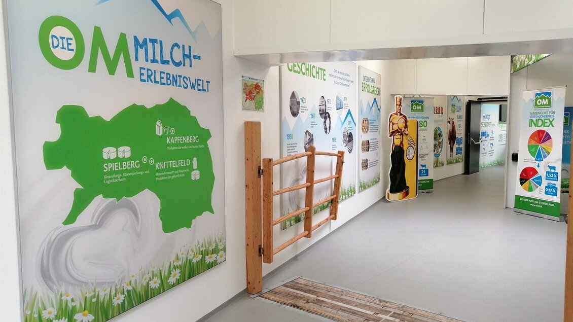 Ein heller Flur mit informativen Wandtafeln über die Milchproduktion. Auf der linken Seite steht ein Bild eines Milchkühe, und der Raum wirkt einladend und edukativ. | © Obersteirische Molkerei