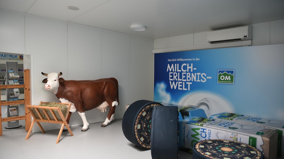Ein Innenraum mit einer Kuhskulptur und verschiedenen dekorativen Elementen. An der Wand befindet sich ein großes Banner mit der Aufschrift "MILCH-ERLEBNIS-WELT". | © Selina Senft