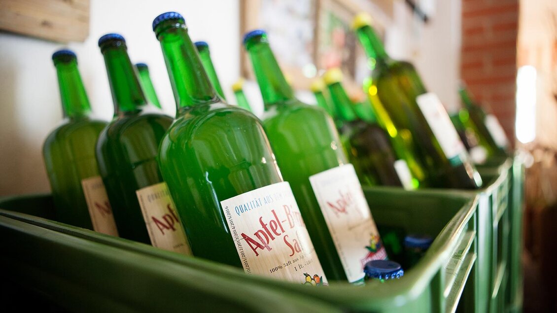 Grüne Flaschen mit Apfelsaft stehen in einem grünen Kasten. Die Flaschen sind gut sichtbar und wirken frisch und einladend. | © Tourismusverband Fürstenfeld