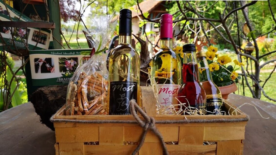 Eine schöne Geschenkkiste mit verschiedenen Getränken, einschließlich Wein und Sirup. Dazu gibt es Brezeln und frische Blumen im Hintergrund. | © Obsthof Braunstein