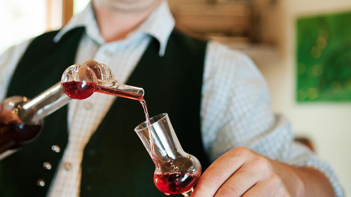Ein Mann in traditioneller Kleidung schenkt einen bunten Likör in ein Glas ein. Die Szene wirkt gemütlich und einladend. | © Tourismusverband Thermen-Vulkanland