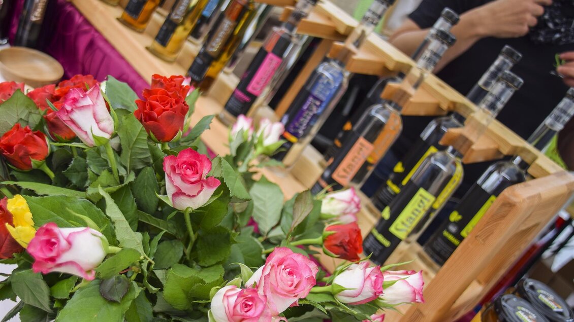 Ein schöner Blumenstrauß mit roten und rosa Rosen steht vor einer Ausstellung von Flaschen. Im Hintergrund sind verschiedene Produkte auf Holzregalen zu sehen. | © Thermen- & Vulkanland Steiermark