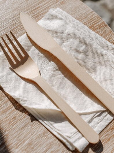 Wooden fork and wooden knife on napkins on a wooden table outdoors – cobblestones in the background | © Midjourney - Benedikt Trummer