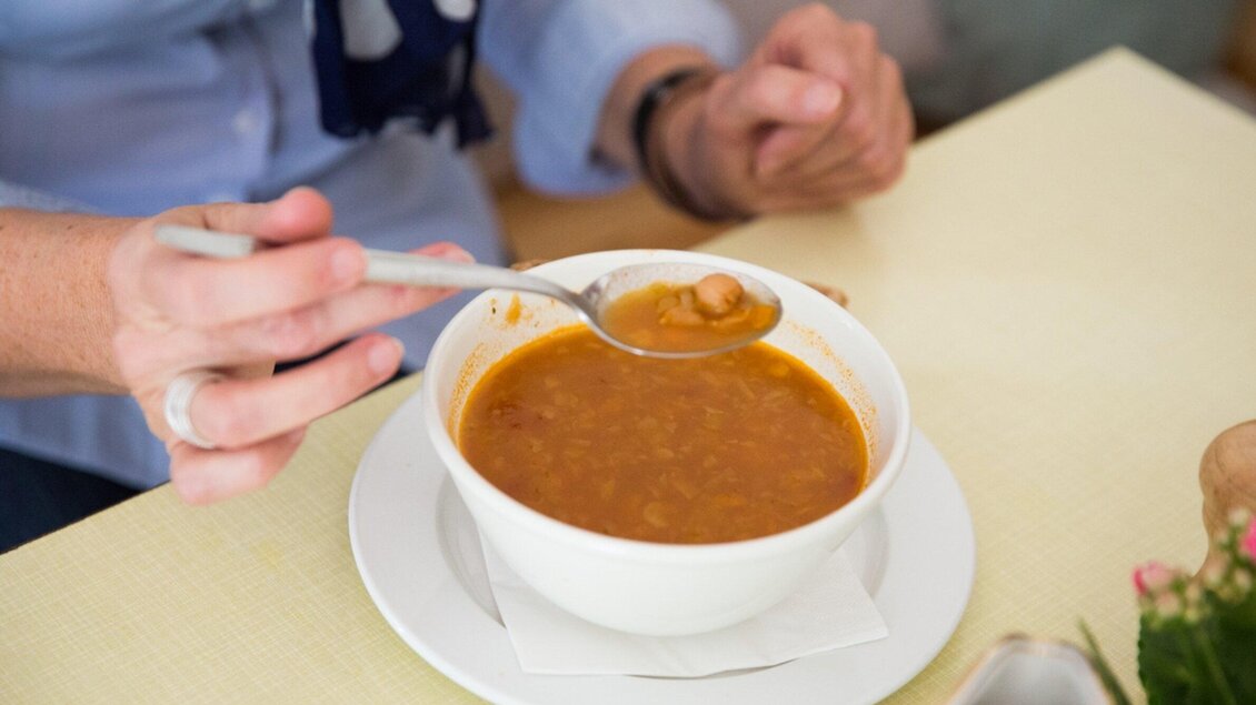Eine Person isst mit einem Löffel aus einer Schüssel mit herzhafter Suppe. Die Suppe hat eine rote Farbe und enthält Bohnen. | © Svetlana Gombats Photography 