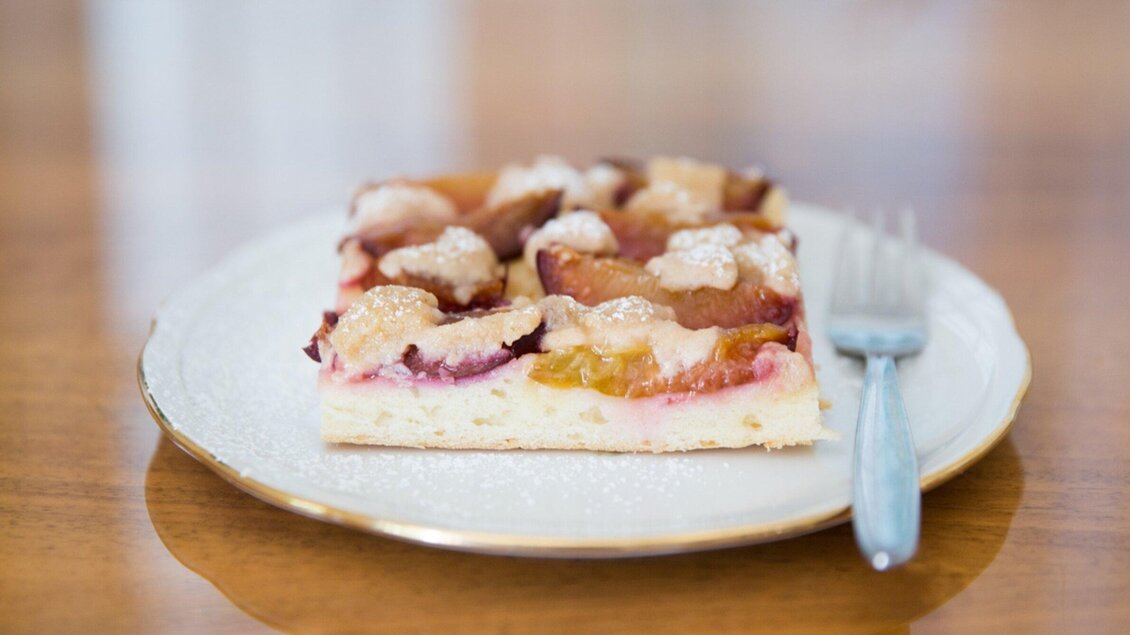 Ein Stück Pflaumenkuchen auf einem weißen Teller. Daneben liegt eine kleine Gabel. | © Omas Teekanne - Svetlana Gombats Photography