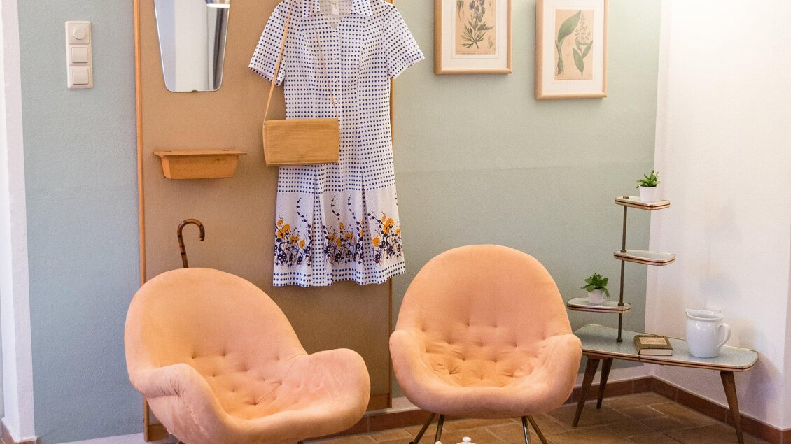Ein stilvoller Eingangsbereich mit zwei rosa Sesseln und einem Kleid. An der Wand hängen Bilder und ein Spiegel. | © Omas Teekanne