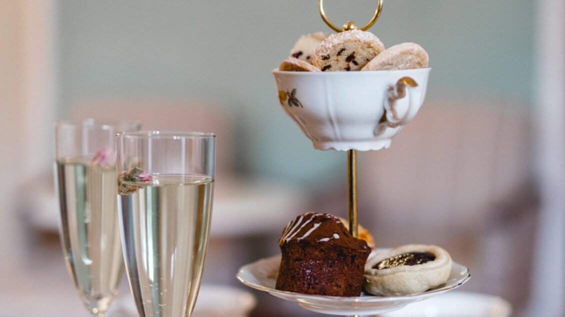 Ein elegantes Desserttablett mit verschiedenen Keksen und einem Muffin. Im Hintergrund stehen zwei Gläser mit Sekt. | © Omas Teekanne