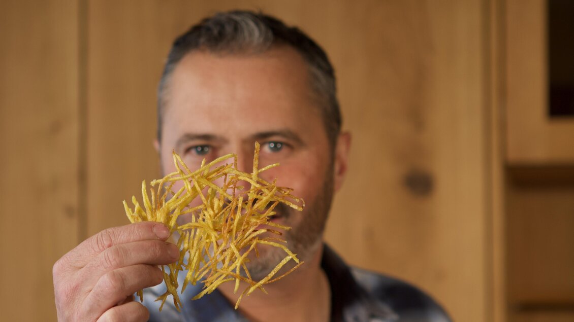 Ein Mann hält gelbe, dünne Zweige in der Hand. Im Hintergrund ist eine Holzfläche zu sehen.