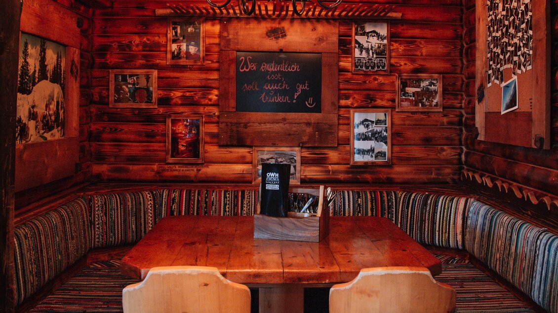 Ein gemütliches Holz-Interieur mit einem großen Tisch und zwei Stühlen. An den Wänden hängen Fotos und eine hübsche Deckenlampe erhellt den Raum. | © OWH