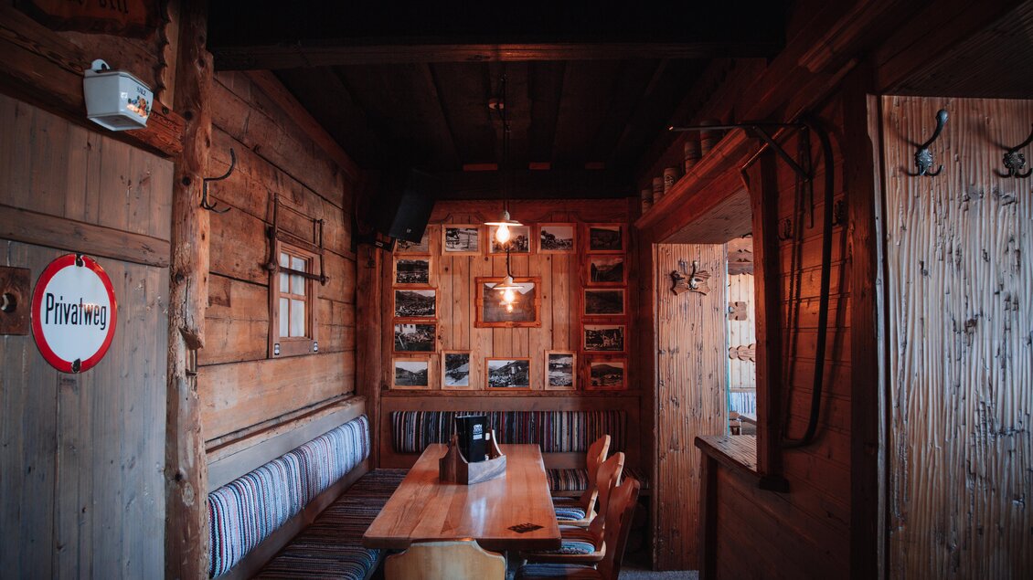 Ein gemütlicher Innenraum mit Holzvertäfelung und einem langen Tisch. An den Wänden hängen historische Fotos, und es gibt eine rustikale Sitzbank. | © OWH