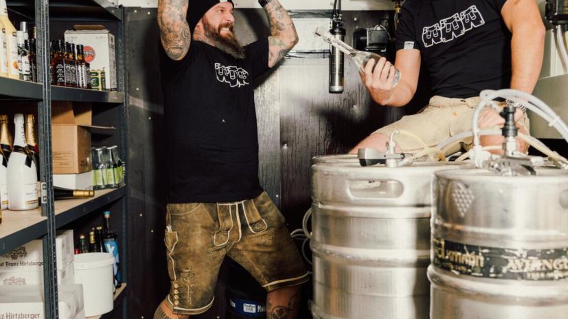 Zwei Männer in einem Lagerraum heben Fässer und haben Spaß. Der Raum ist voller Getränkekästen und es gibt eine industrielle Atmosphäre. | © OWH