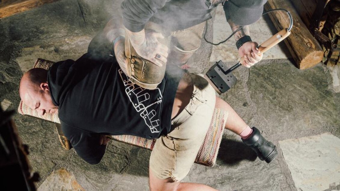 Es sieht aus, als ob eine Person auf einem Tisch liegt, während eine andere Person mit einem Werkzeug beschäftigt ist. Dampf steigt auf, was auf Aktivität und möglicherweise eine Art von Handwerk hinweist. | © OWH