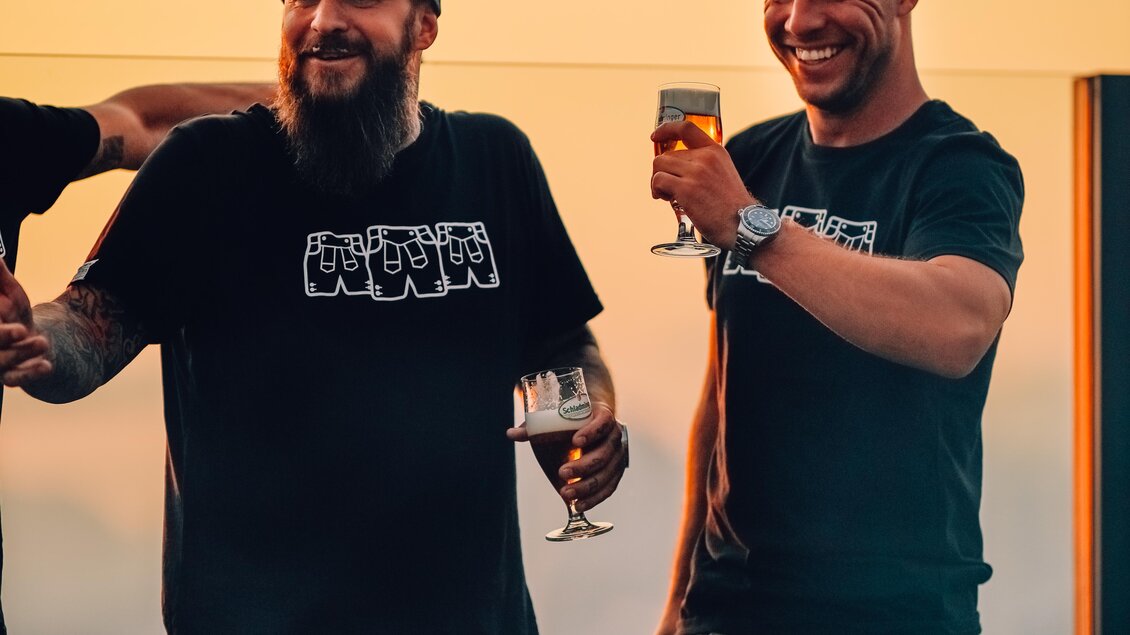 Zwei Männer stehen neben einem Grill und lachen. Sie halten Drinks in der Hand und genießen den Abend. | © OWH