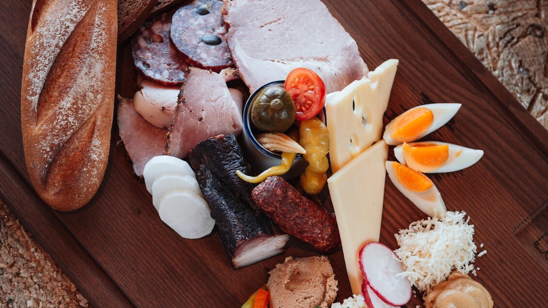 Ein rustikales Holzbrett mit verschiedenen Fleisch- und Wurstsorten, Käse und frischem Gemüse. Dazu ein Glas Bier und ein Schuss Schnaps. | © OWH