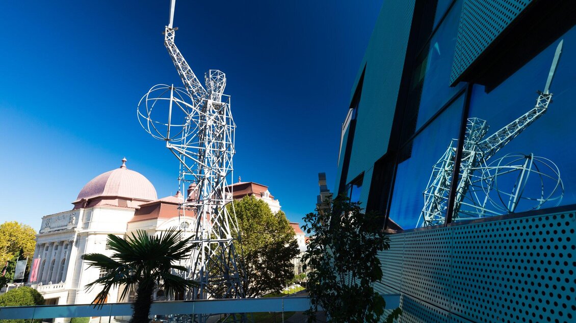 Eine moderne Skulptur mit Lichtschwert aus Metall steht vor der Oper in Graz. Im Hintergrund ist ein klarer blauer Himmel zu sehen. | © Graz Tourismus - Harry Schiffer