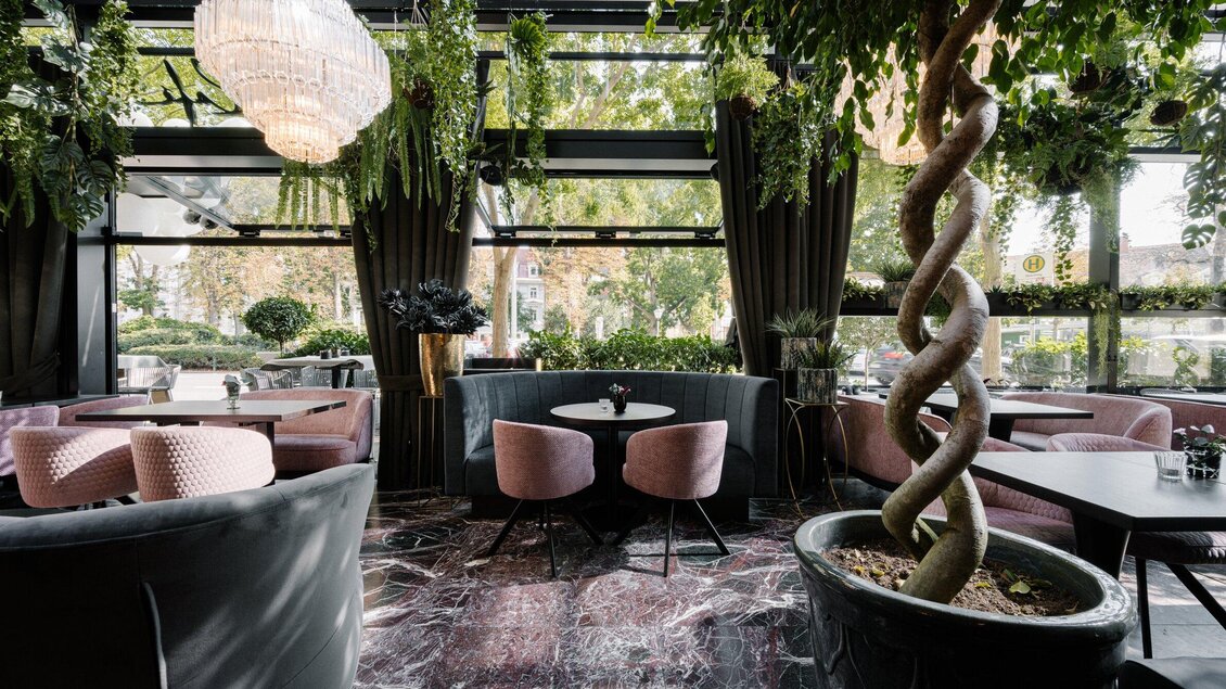 Ein elegantes Café mit modernen Möbeln und vielen Pflanzen. Große Fenster lassen viel Licht herein und schaffen eine angenehme Atmosphäre. | © Operncafé - Joel Kernasenko