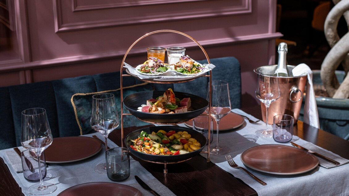 Ein elegantes Tischarrangement mit einem mehrstöckigen Servierstand, der köstliche Gerichte präsentiert. Umgeben von stilvollen Gläsern und einem Sektkühler auf einem festlich gedeckten Tisch. | © Operncafé - Jauk Katharina