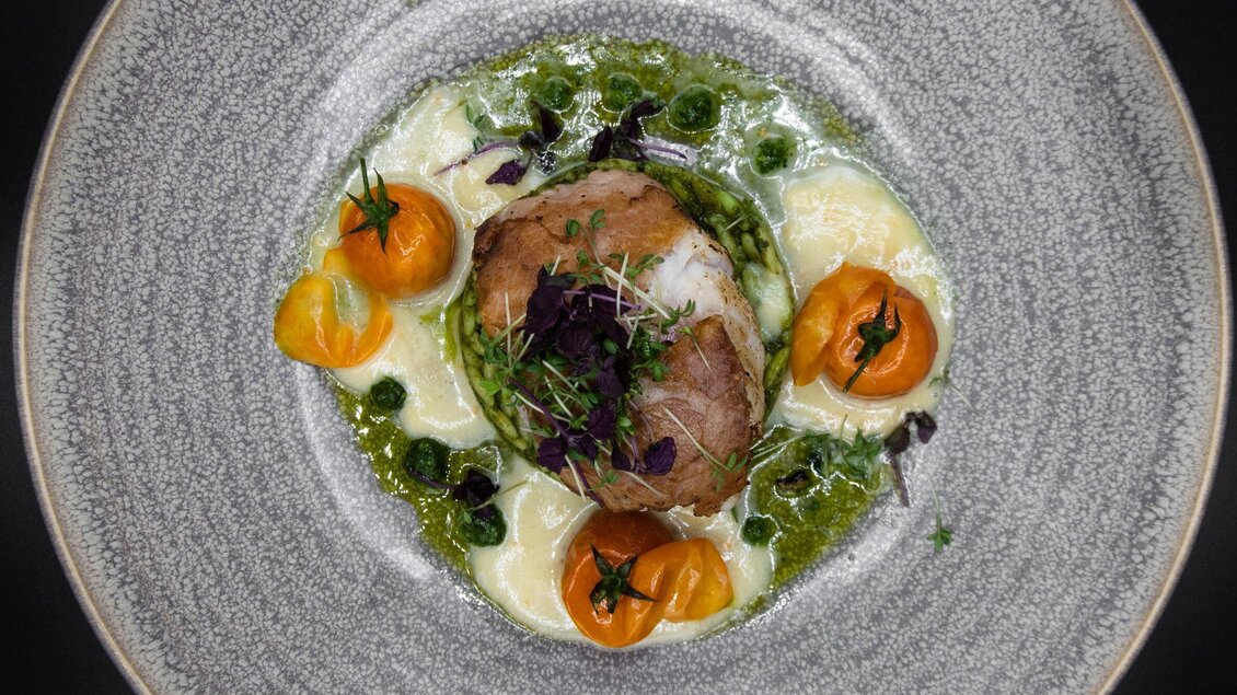 Ein kunstvoll angerichteter Teller mit Fleisch, garniert mit gelben Tomaten und Kräutern. Die Soße umgibt das Gericht und verleiht ihm eine ansprechende Optik. | © Operncafé - Jauk Katharina