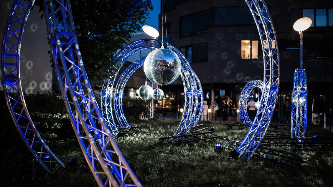 Künstlerische Lichtinstallation mit Spiegelkugeln und Bögen auf einer Grünfläche bei Nacht | © Alex Koch