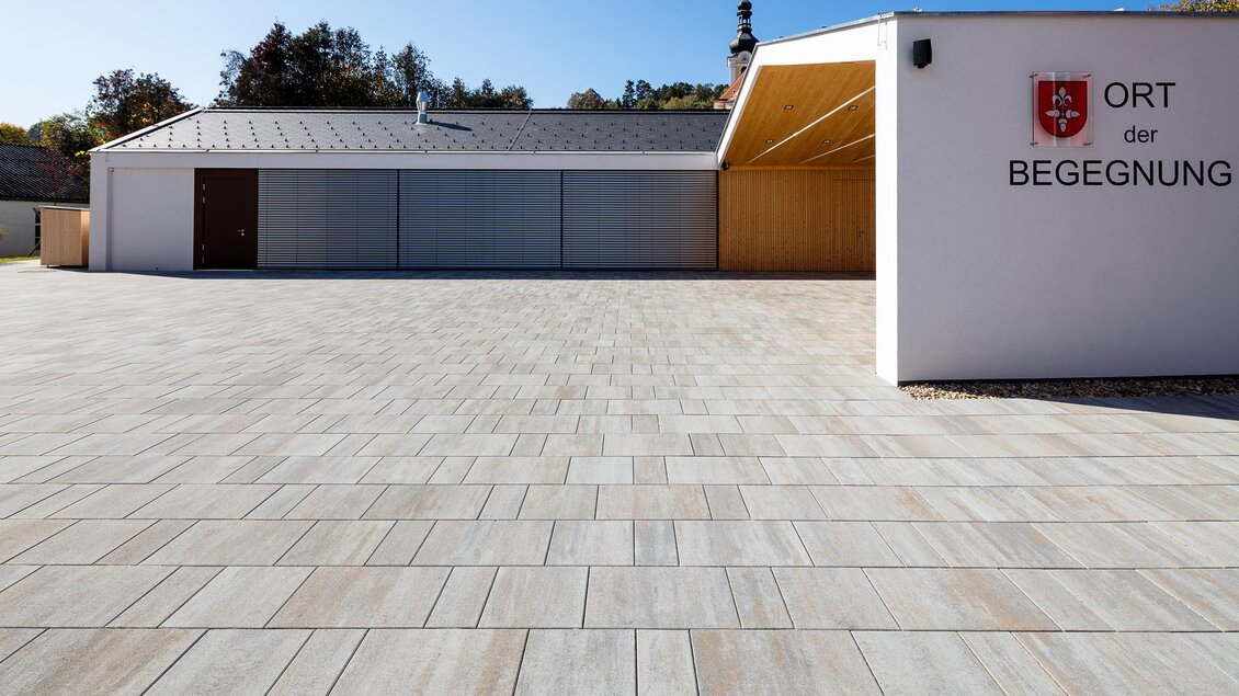 Ein modernes Gebäude mit einem großzügigen Platz aus Fliesen. Im Hintergrund ist eine begrüßte Umgebung zu sehen. | © Gemeinde Bad Blumau/Markus Kaiser